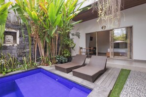 Un área de piscina con sillones de descanso, un muro de piedra y plantas tropicales.