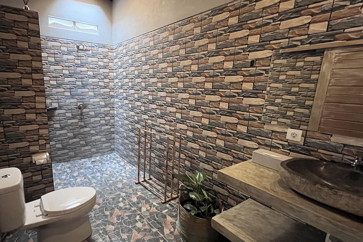 Ein Badezimmer mit Steinwand, Toilette, Waschbecken und Dusche.