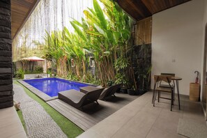 Piscina con sillas de descanso, rodeada de plantas tropicales y un muro de piedra.