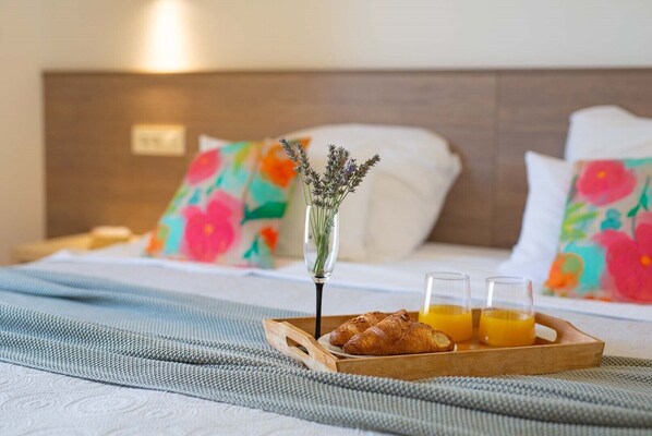 Een netjes opgemaakt bed met bloemenkussens, een dienblad met croissants en sinaasappelsap, en een vaas met lavendel.