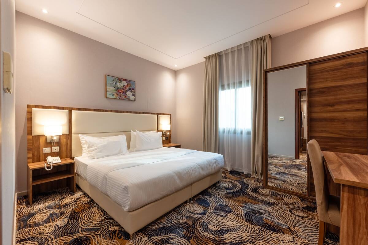 A hotel room with a large bed, bedside lamps, a desk, and a patterned carpet.
