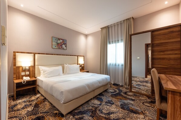 A hotel room with a large bed, bedside lamps, a desk, and a patterned carpet. - GH HOTEL (Madinah)
