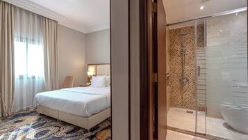A hotel room with a bed, a bathroom with a shower, and a patterned carpet.