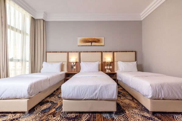 A hotel room with three single beds, a large window with curtains, a wall-mounted artwork, and a patterned carpet. - GH HOTEL (Madinah)