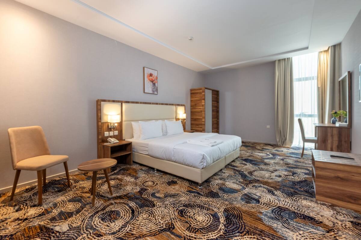 A hotel room with a large bed, a desk, a chair, and a patterned carpet.