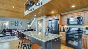 A modern kitchen with a central island, bar stools, a refrigerator, stove, and a microwave. - Charming 4-bedroom home with WiFi, game room and more near Wintergreen Resort!   (Nellysford)