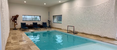 An indoor swimming pool with tiled flooring, lounge chairs, and a decorative wooden sculpture.