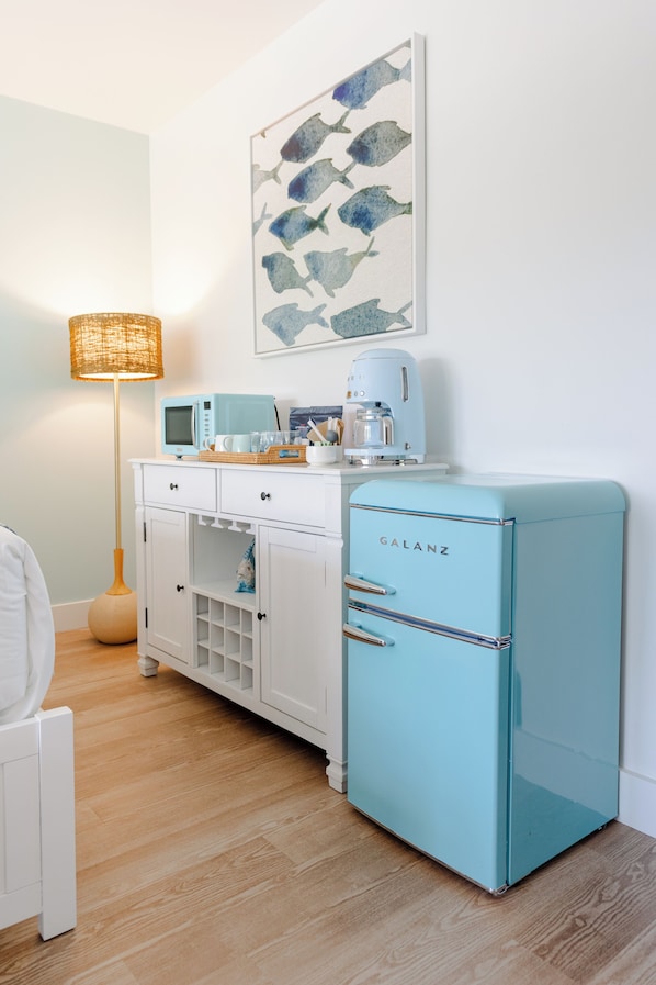 Una kitchenette con un armario blanco, un refrigerador azul, un microondas y una cafetera.