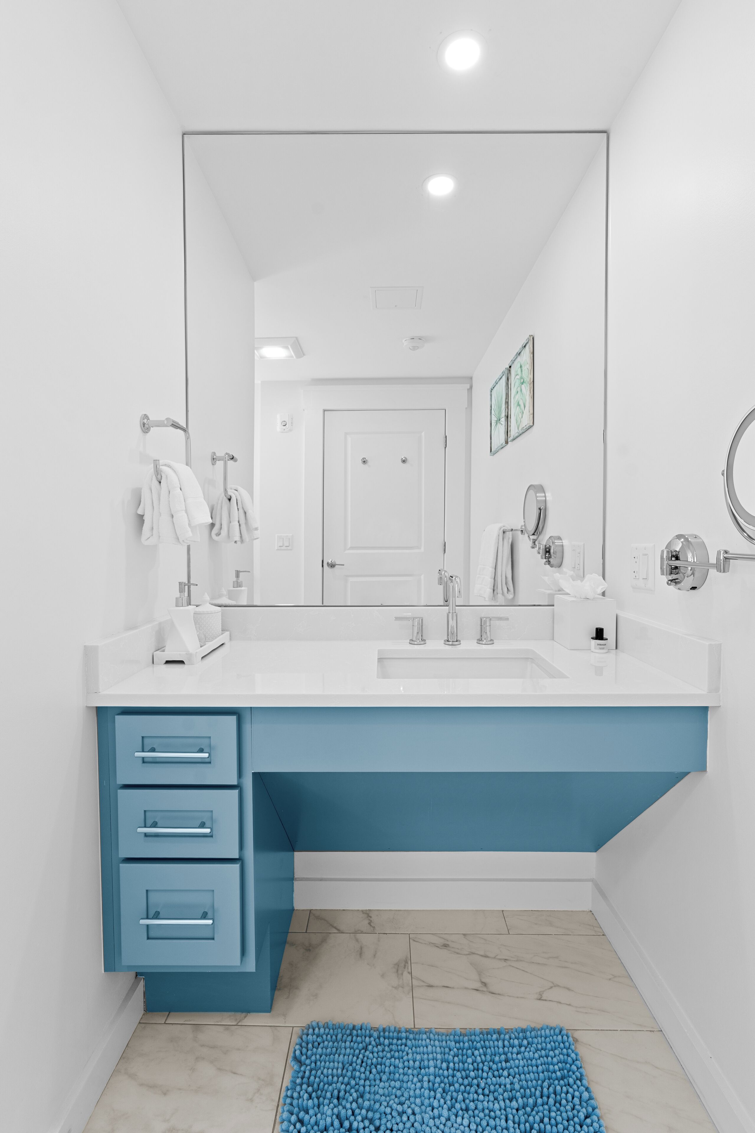Une salle de bain moderne avec un meuble-lavabo blanc et bleu, un grand miroir et un tapis de bain bleu.