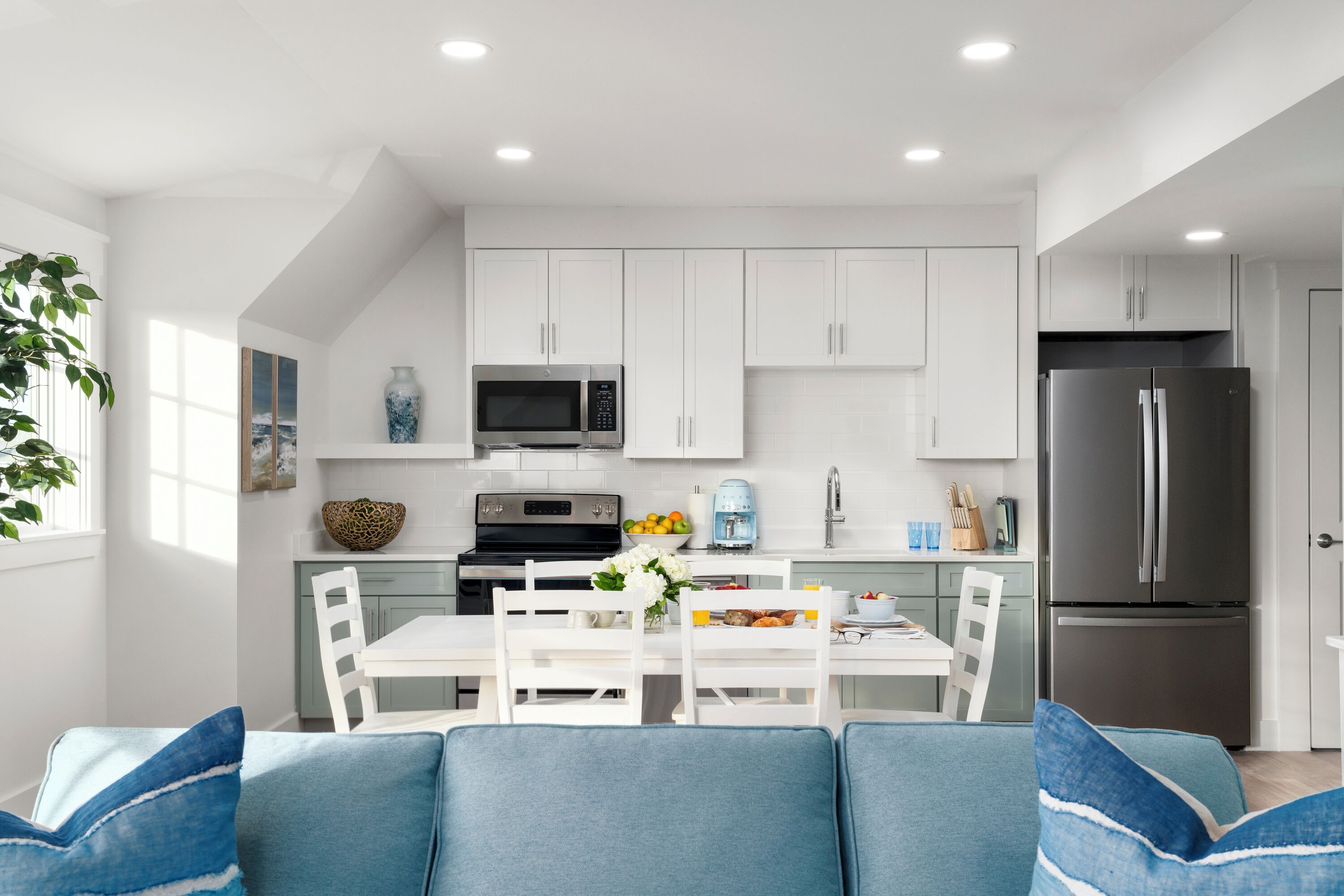 A modern kitchen with white cabinets, a stainless steel refrigerator, and a dining area with a white table and chairs.