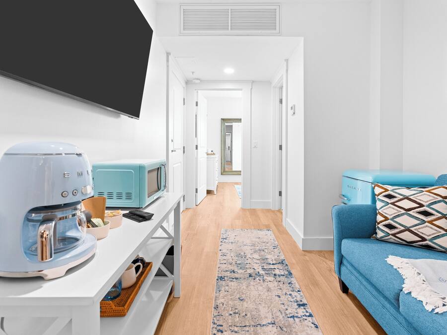 A modern living room with a coffee maker, a blue sofa, and a TV on the wall.