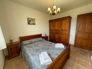 A bedroom with a wooden bed, a nightstand, a dresser, a chandelier, and a painting on the wall.