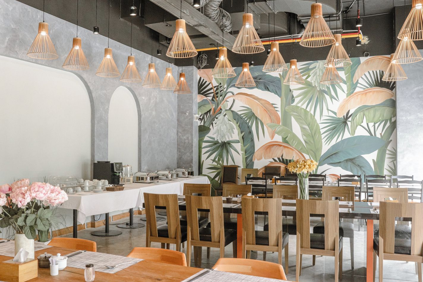 Ein Restaurant mit mehreren Tischen und Stühlen, mit Bambuspenderleuchten und einer großen, tropischen Wandmalerei.