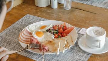Un plato de desayuno con huevos, tomates y jamón, una taza de café y un tenedor sobre una mesa de madera.