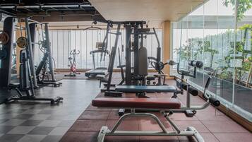 Et fitnesscenter med forskellig træningsudstyr, store vinduer og et skakternet gulv.
