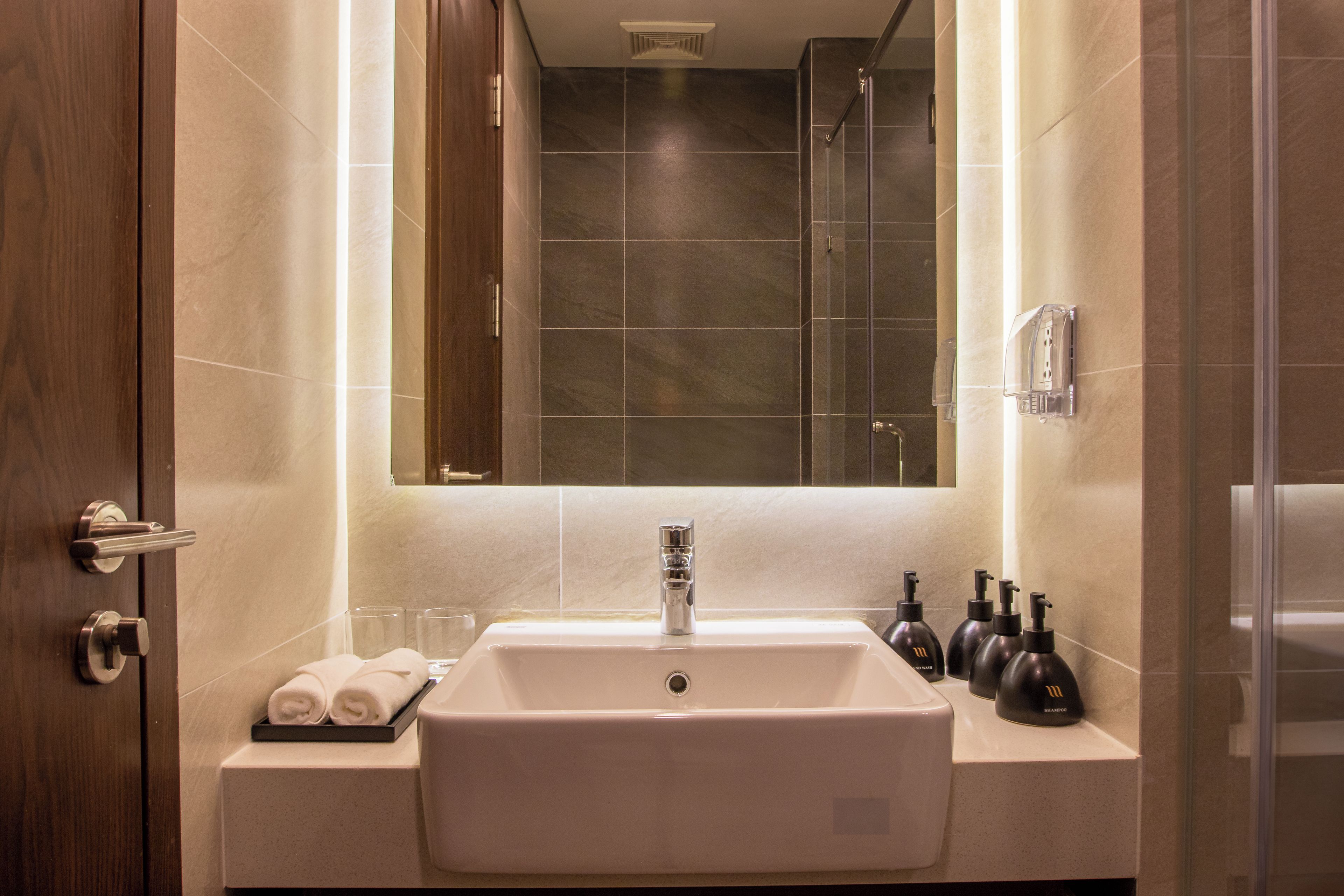 A bathroom with a large mirror, a sink, and a shower. There are towels and toiletries on the counter.