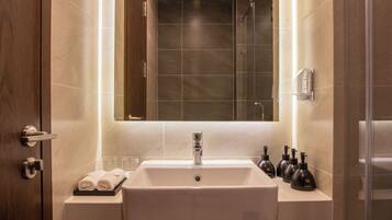 A bathroom with a large mirror, a sink, and a shower. There are towels and toiletries on the counter.