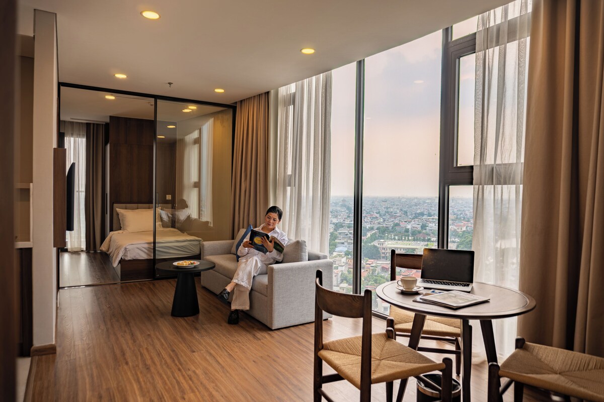 Una habitación de hotel moderna con una cama grande, un sofá, una mesa de comedor y una computadora portátil.