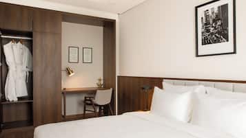 Habitación de hotel con cama, escritorio, silla, armario y un cuadro en la pared.