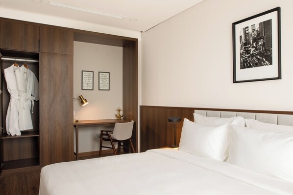 Habitación de hotel con cama, escritorio, silla, armario y un cuadro en la pared.