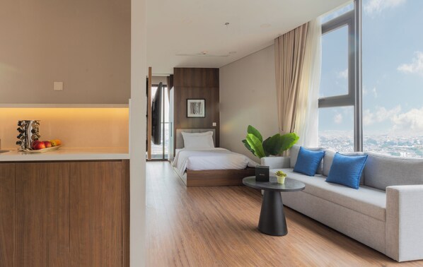 A modern hotel room with a bed, a sofa, a dining area, and a large window offering a city view. - Mandala Hotel & Suites Hai Duong (Tan Hung Ward, Hai Phong City)