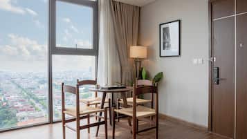 Et hotelværelse med et stort vindue, et rundt bord med stole, en lampe og en dør.