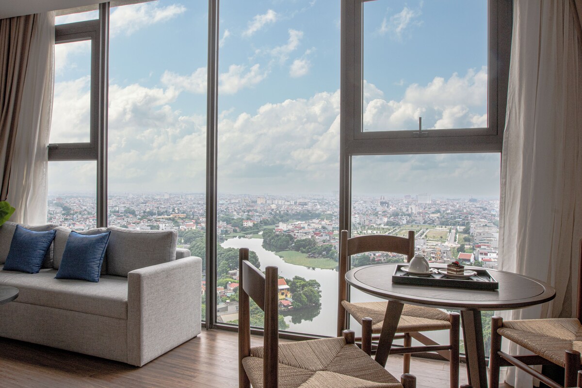 Una sala de estar moderna con un ventanal que ofrece vistas de la ciudad, un sofá con cojines y una mesa redonda con bandeja.