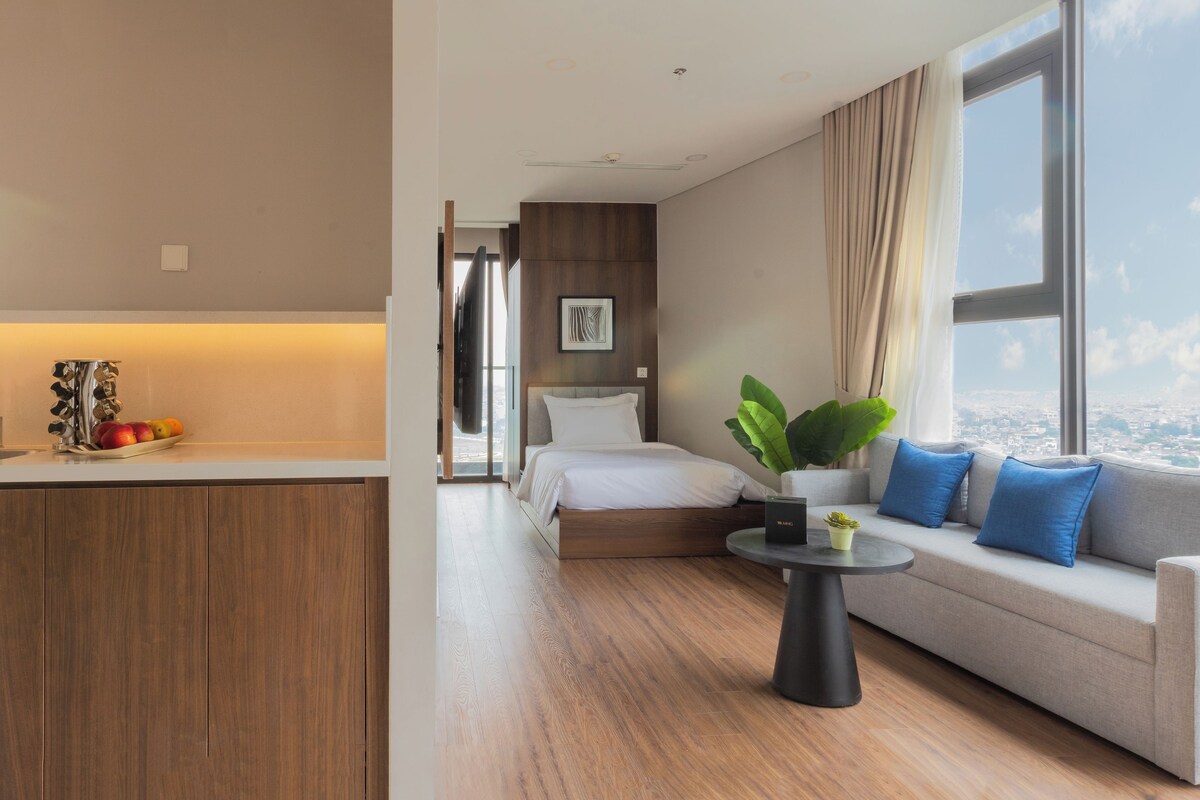 Una habitación de hotel moderna con cama, sofá, zona de comedor y un amplio ventanal con vistas a la ciudad.