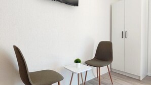 Una camera moderna con una TV a schermo piatto montata a parete, due poltrone, un tavolino con una pianta e un armadio.