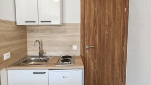 Una cucina compatta con lavandino, fornello e due pensili bianchi.