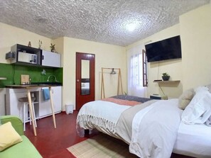 A bedroom with a bed, a desk, a chair, a mirror, a wardrobe, and a television.