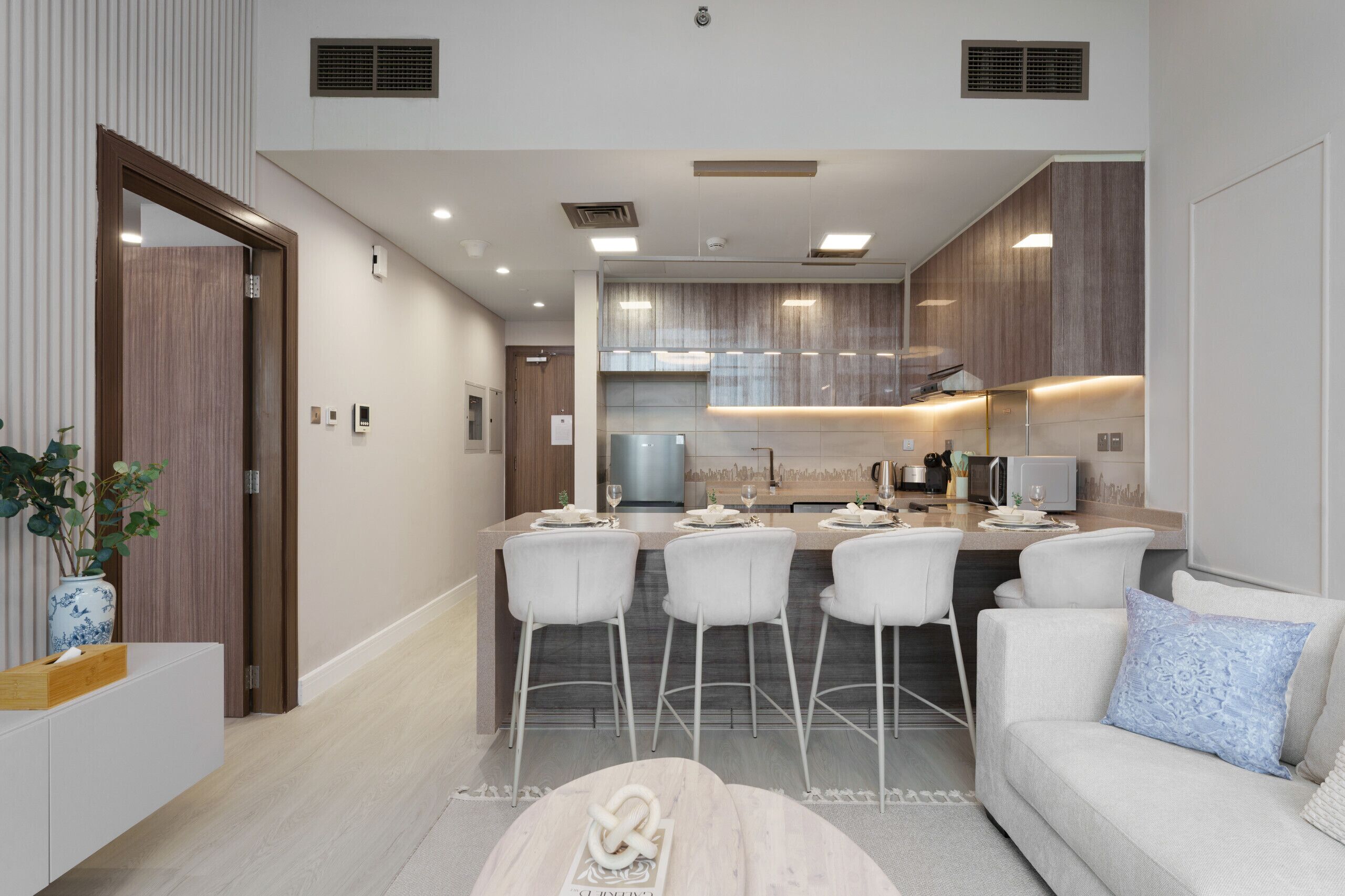 A modern kitchen with a central island, bar stools, and a dining area with a sofa and coffee table.