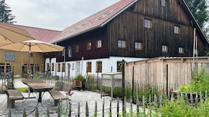 En rustik utomhusplats med träbord och träbänkar, omgiven av en trädgård med röda blommor och ett trästaket.