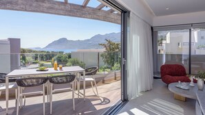Ein moderner Balkon mit Tisch, Stühlen, einem roten Sessel und einer Glastür zum Zimmer.