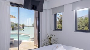 Ein modernes Hotelzimmer mit einem großen Bett, einem an der Wand montierten Fernseher und einer Schiebetür zu einem Balkon mit einem Pool.