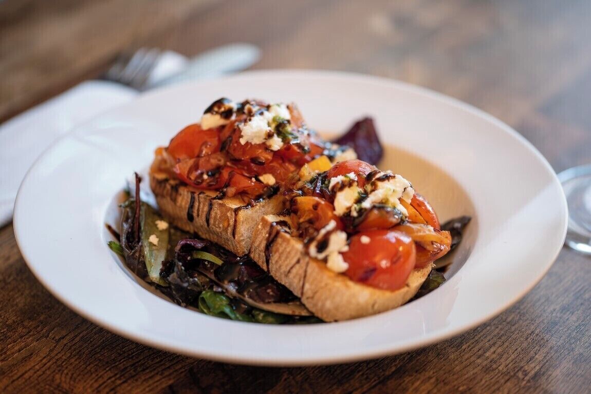 A plate of food with grilled meat, tomatoes, and greens on a wooden table.