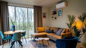 A modern living room with a sofa, chairs, a dining table, and a large window with curtains. - Chalet on a Holiday Park 3.5 km From the Beach (De Cocksdorp)