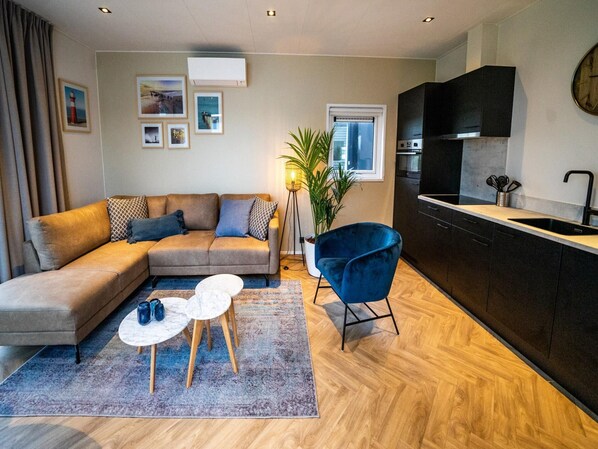 Una sala moderna con un sofá, una mesa de centro y un sillón azul. Hay una cocina con encimera negra y un fregadero.