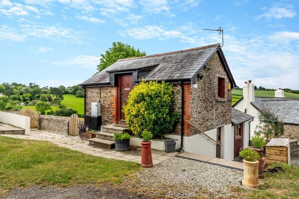 A stone house with a red door, a small garden with potted plants, and a gravel pathway.