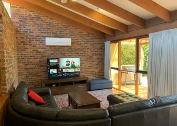 Una sala de estar con pared de ladrillo, televisor, sofá y puerta corrediza de vidrio que da al exterior.