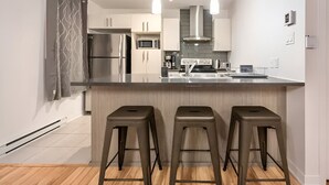 Een moderne keuken met roestvrijstalen apparatuur, een centraal kookeiland met barkrukken en een grijze betegelde spatwand.