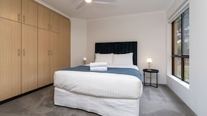 Een slaapkamer met een bed, een plafondventilator, een raam en een kledingkast.
