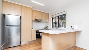 Een moderne keuken met houten kastjes, een roestvrijstalen koelkast, een inbouwoven en een groot raam voor natuurlijk licht.