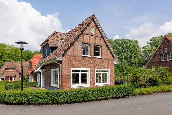 Een tweelaags huis met een bakstenen gevel, ramen met witte kozijnen en een schuin dak.