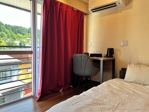 A hotel room with a bed, a desk with a chair, a red curtain, and an air conditioning unit. - Jinya Sunset Inn by Murasaki (Takayama)