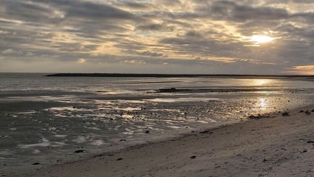 Una spiaggia con un'ampia riva sabbiosa e acque calme.