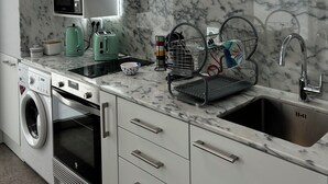 A modern kitchen with white cabinets, a built-in microwave, a stainless steel sink, and a dish drying rack.