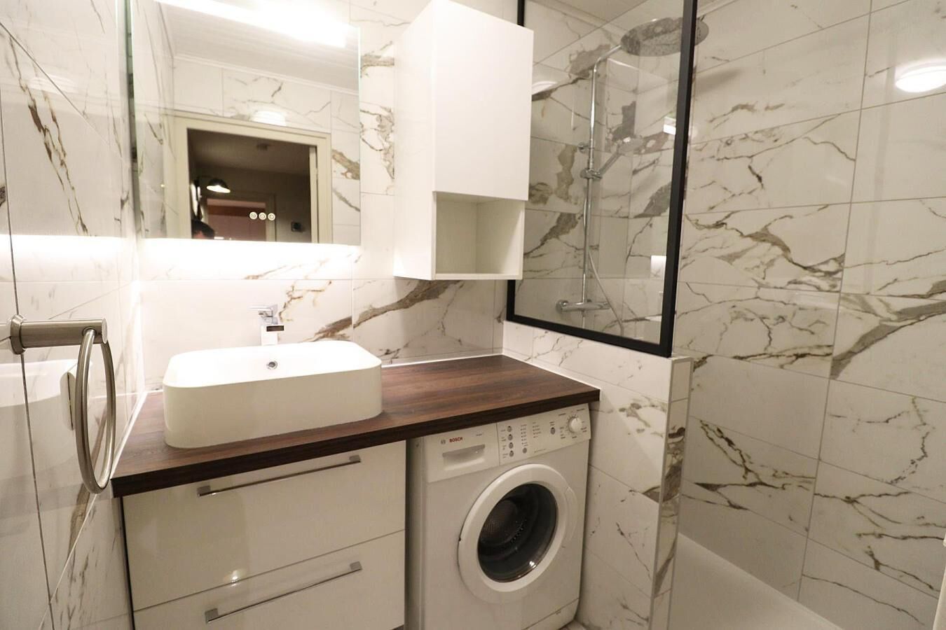 A modern bathroom with a white sink, a Bosch washing machine, and marble-patterned walls.