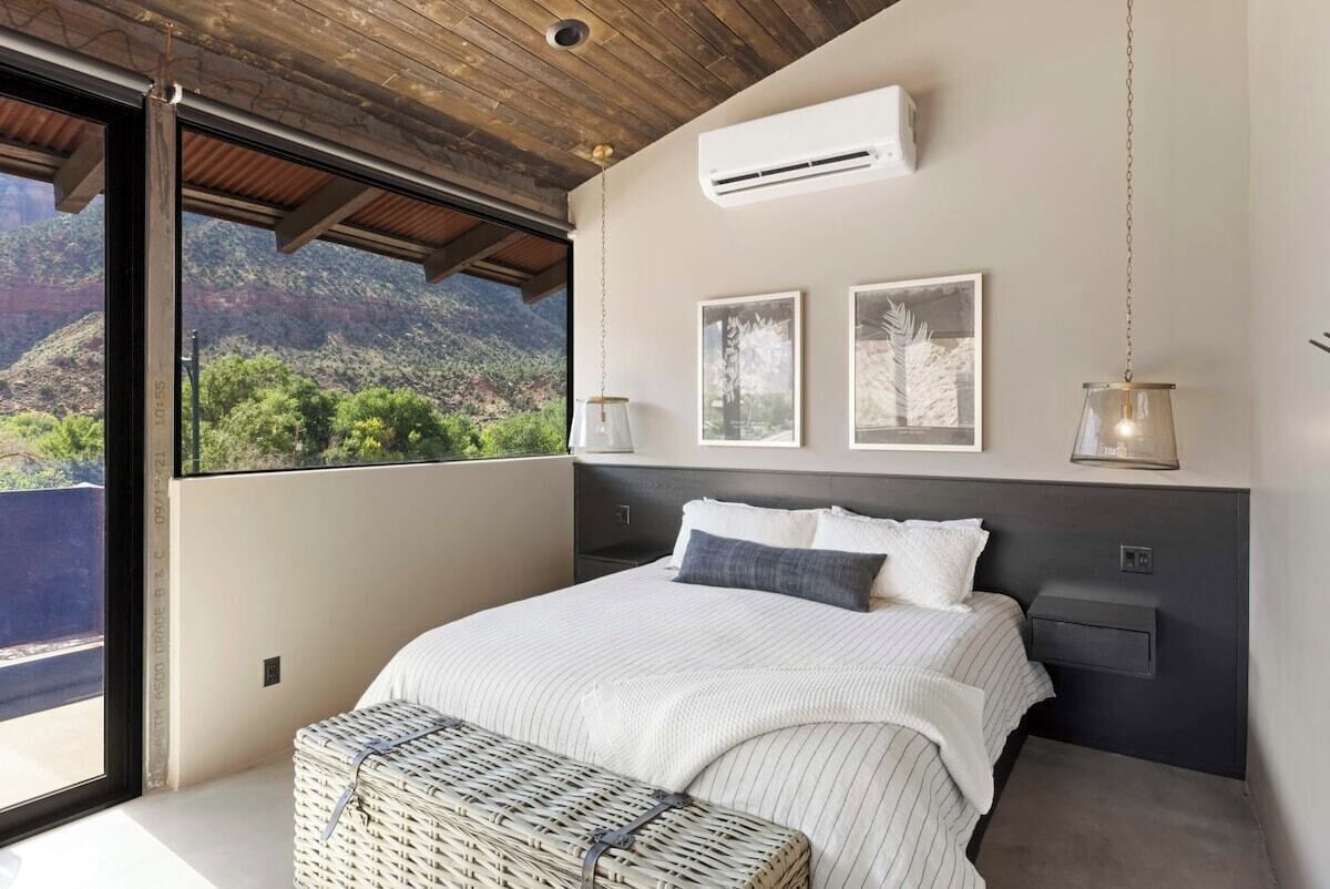 Una camera da letto con un'ampia finestra, un letto con biancheria da letto bianca, due quadri appesi al muro e un lampadario.