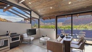 Una cocina moderna con electrodomésticos integrados, una zona de estar con sofá y sillones, y grandes ventanales con vistas a las montañas.